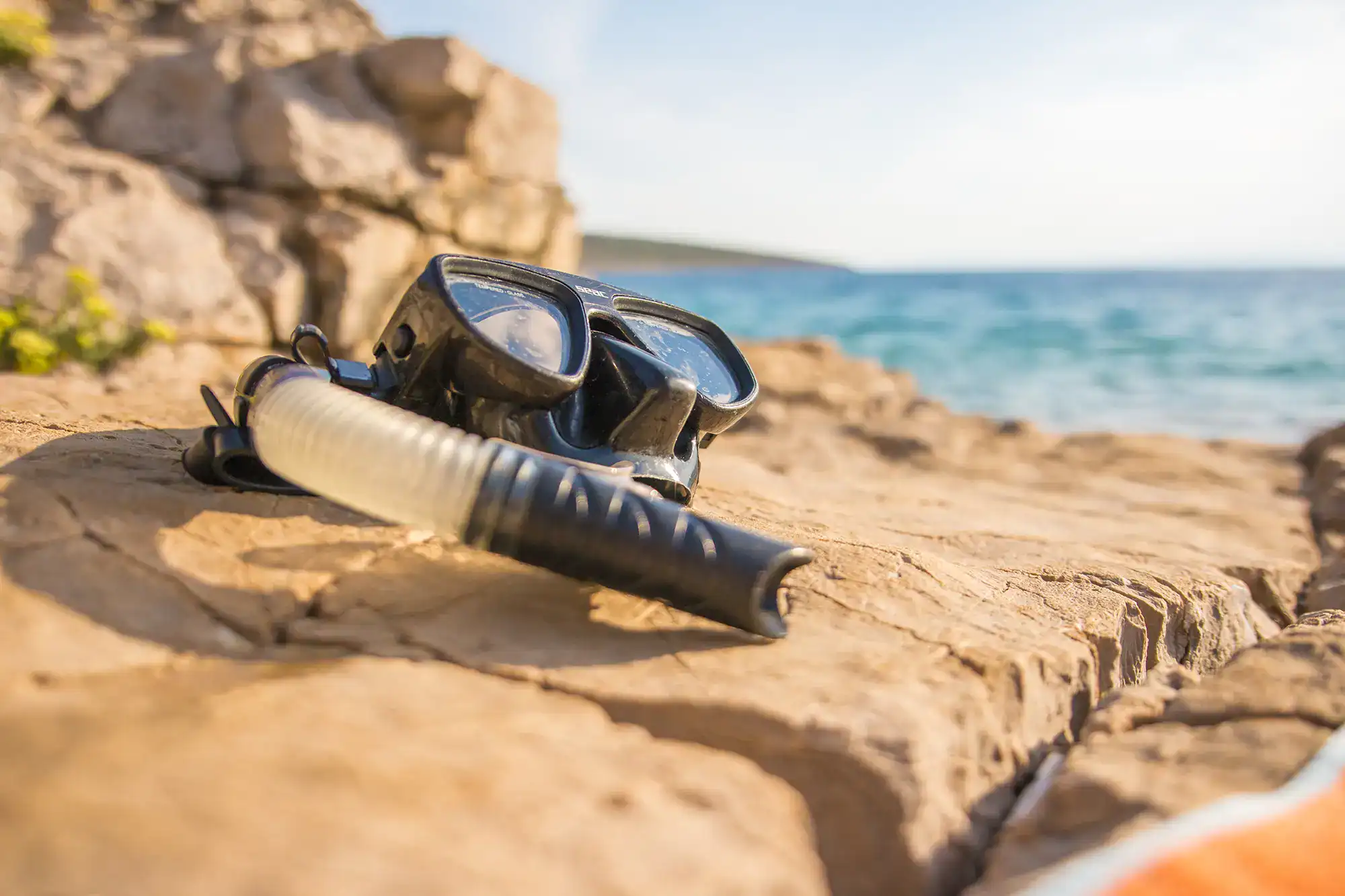 Taucherbrille auf Felsen am Strand mit Blick aufs Meer, ideal für Schnorcheln und Tauchen.