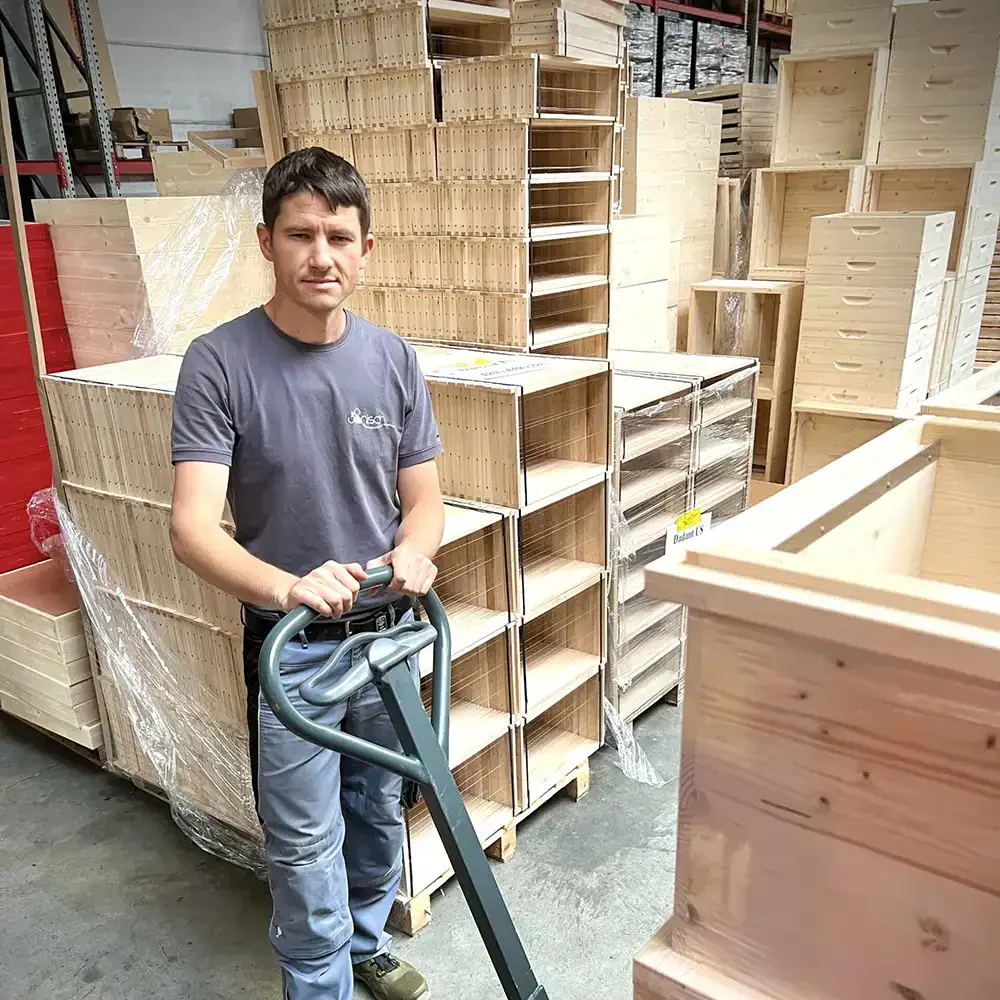 Imker bei der Arbeit in der Bienenhaltung, mit Holzbeuten im Lager.